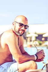 Wall Mural - Portrait of a  happy smiling bearded Man holding   a Glass of rose Wine by the swimming pool on the empty deck of a cruise liner.Vacation and travel conceptl