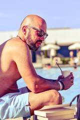 Wall Mural - Portrait of a  happy smiling bearded Man holding   a Glass of rose Wine by the swimming pool on the empty deck of a cruise liner.Vacation and travel conceptl