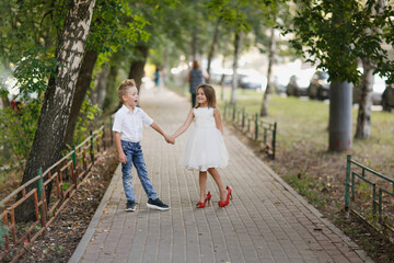 Cute couple kids boy and girl hold hands on walk in summer. Girl child in high heels, kids play date