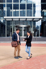 caucasian man and asiatic woman talking about business in front of the entrance to an office building, concept of coworkers and lifestyle, copy space for text