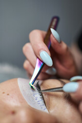 two tweezers close-up with eyelash extensions. one pushes, the other sticks. a special patch is glued under the eye