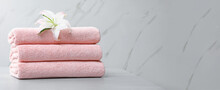 Stack Of Folded Pink Towels With White Lily On Table Against Light Background, Space For Text. Banner Design