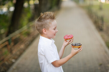 Boy child holds 2 donuts in his hands, pink and chocolate donuts in children's hands