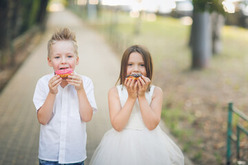 Cute romantic couple of kids with donuts. Brother and sister twins eat pink and chocolate donuts in summer outdoor