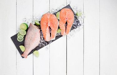 Wall Mural - Red fish steak and sea bass on a black stone board on a white table with lime slices and ice. Trout steak on a stone board with perch. Healthy food, seafood