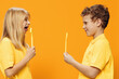 happy children, brother and sister, stand in bright yellow clothes sideways to the camera and joyfully laugh looking at each other. Studio horizontal photography on orange background