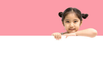 Wall Mural - Happy little Asian child girl smiling and showing white blank sign billboard isolated on pink background.