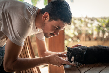 close up. young man interacts with a a black cat in a garden