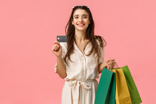Happy Caucasian Brunette Woman In Stylish Dress, Carry Shopping Bags And Credit Card, Paying Everything With Paypass, Have Special Discount, Using Bank Deposit, Standing Pink Background