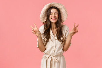 Wall Mural - Happiness, cheer and joy concept. Silly good-looking tender, feminine girlfriend in hat and dress, showing peace signs and laughing carefree, enjoying vacation, being on trip, pink background