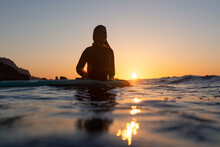 Surfer Girl Waiting For A Wave In The Water At Sunset