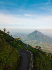 Wall Mural - Drone photo of the road on the slopes of a mountain and surrounded by dense forest with Andong Mountain on the background. It located in Mount Telomoyo in clear weather, central java, Indonesia