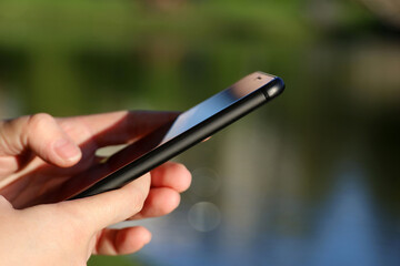 Female hands with smartphone close up on lake background. Woman using mobile phone in summer park