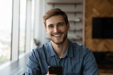 Head Shot Of Happy Young Millennial Man Holding Smartphone, Looking At Camera, Smiling, Laughing. Portrait Of Positive Customer, Smartphone User Satisfied With Online App, Virtual Service Work