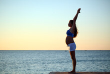 Pregnant Girl Doing Yoga On The Seashore In The Morning Against The Sky And Water