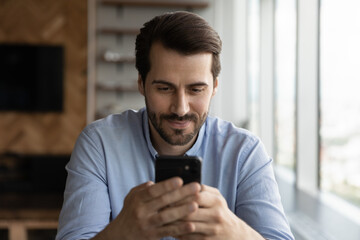 Wall Mural - happy millennial man using app on smartphone, making telephone call, reading, texting, smiling at sc