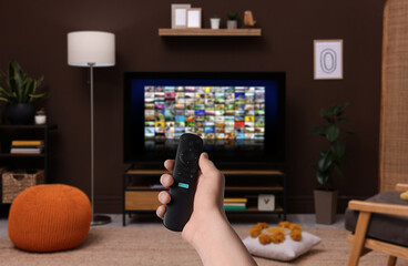 Wall Mural - Woman with remote control changing channels while watching TV at home, closeup