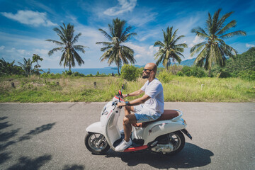 Wall Mural - Stylish young man rides a motorbike on the road near the sea and palm trees