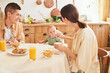 A young Caucasian family with a baby have breakfast in the kitchen.