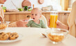 A father feeds his one-year-old baby yogurt, a family breakfast.