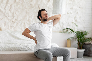 Unhappy man suffering from back pain at home in bedroom