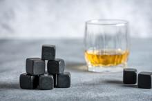 Closeup Of Whiskey Stones And A Glass Of Whiskey On A Gray Concrete Table. Side View, Selective Focus.