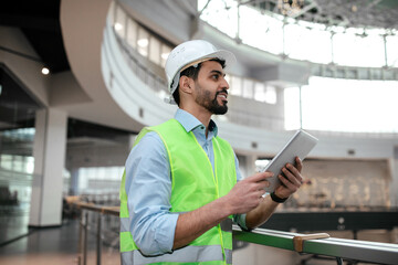 Wall Mural - Glad millennial middle eastern man engineer in protective uniform and hardhat with beard hold tablet