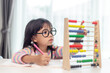 A young cute Asian girl is using the abacus with colored beads to learn how to count at home