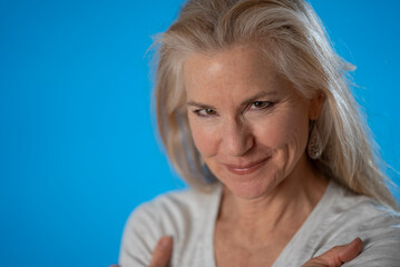 Closeup portrait of happy smiling mature woman crossing arms isolated on blue background studio eyes toward product sale. People lifestyle concept