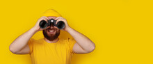 Smiling Man Looking Into Binoculars Over Yellow Background, Panoramic Layout