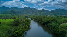 Aerial View Landscape With Mountains, Forest And A River Beautiful Scenery, Tree Lined Foliage On Both Sides Of The River Flowing Through The Rural Countryside And Hills.