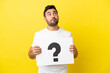 © luismolinero - Young handsome caucasian man isolated on yellow background holding a placard with question mark symbol and thinking