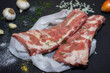 Raw pork meat on a black background from above, in the background garlic and onions. The meat is prepared for marinating and frying