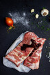 Raw pork meat on a black background from above, in the background garlic and onions. The meat is prepared for marinating and frying