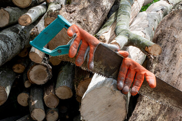 A rusty metal hacksaw with old working orange gloves saws a wooden log