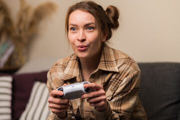 Wall Mural - A fair-haired pretty girl with a joystick emotionally plays a video game. Online games with friends, communication, hobbies, passion, virtual reality, cyberspace, video games.