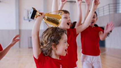 Wall Mural - School sports teammates rising up golden trophy after winning sports indoor competition