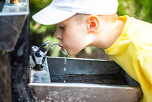 Close-up Of A Boy  Drinking Water From An Outdoor Water Fountain In A Park
