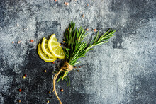 Overhead View Of Rosemary And Lemon Slices On A Grey Background With Peppercorns And Pink Salt