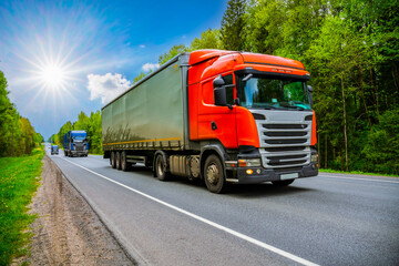 Transportation goods. Trucks are on a road into forest in a sunny summer day.