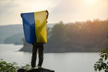 Rear view of a woman standing by a river holding a Ukrainian flag above her head, Thailand