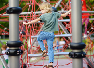 Cute preschooler boy having fun on outdoor playground. Spring summer autumn active sport leisure for kids. Activity for family with children. Equipment of entertainment.