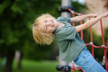 Wall Mural - Cute perky preschooler boy having fun on outdoor playground. Spring or summer or autumn active sport leisure for kids. Outdoor activities for family with children.