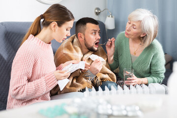 Family taking care of man with cold at home, giving medicines and drinks.