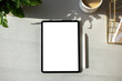 Digital tablet with blank screen mockup, pen, cup of coffee, plant on home office desk table. Freelancer workspace top view.