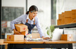 © David - Young Asian entrepreneur SME woman checking product on stock take note with a laptop. Small business owner working at home. Check address on the parcel SME online start up freelance concept.