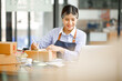 © David - Young Asian entrepreneur SME woman checking product on stock take note with a laptop. Small business owner working at home. Check address on the parcel SME online start up freelance concept.