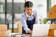 © David - Young Asian entrepreneur SME woman checking product on stock take note with a laptop. Small business owner working at home. Check address on the parcel SME online start up freelance concept.