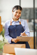 © David - Young Asian entrepreneur SME woman checking product on stock take note with a laptop. Small business owner working at home. Check address on the parcel SME online start up freelance concept.