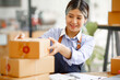 © David - Young Asian entrepreneur SME woman checking product on stock take note with a laptop. Small business owner working at home. Check address on the parcel SME online start up freelance concept.